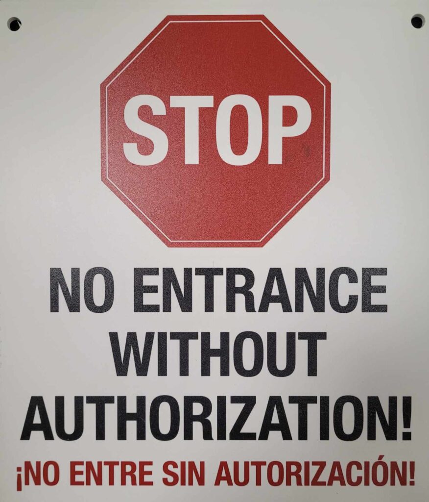 The image shows a red octagonal stop sign with the text "STOP" in white. Below the stop sign, there is text in black that says "NO ENTRANCE WITHOUT AUTHORIZATION!" and the Spanish translation "¡NO ENTRE SIN AUTORIZACIÓN!". The sign is intended to restrict access to an area or facility without proper authorization.