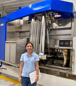Nesli Akdeniz stands in front of an automatic milking system.
