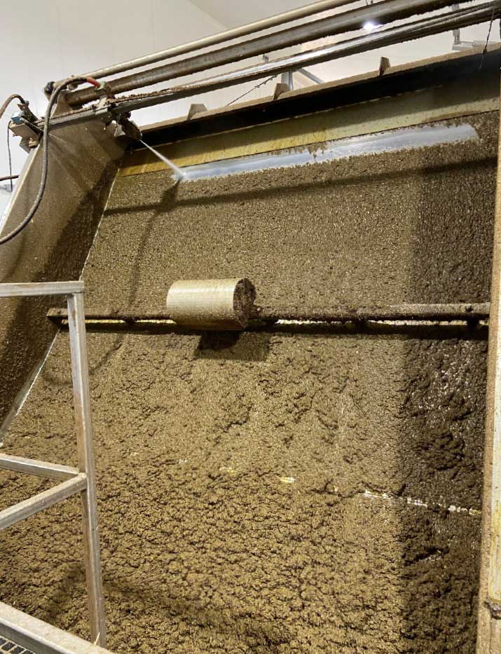 Sloped screen separator machine processing dairy manure, showing wet solids accumulating on an angled metal screen with a cylindrical outlet pipe visible.